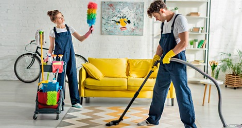 Two individuals are tidying up a room featuring a bright yellow couch, creating a clean and organized space.