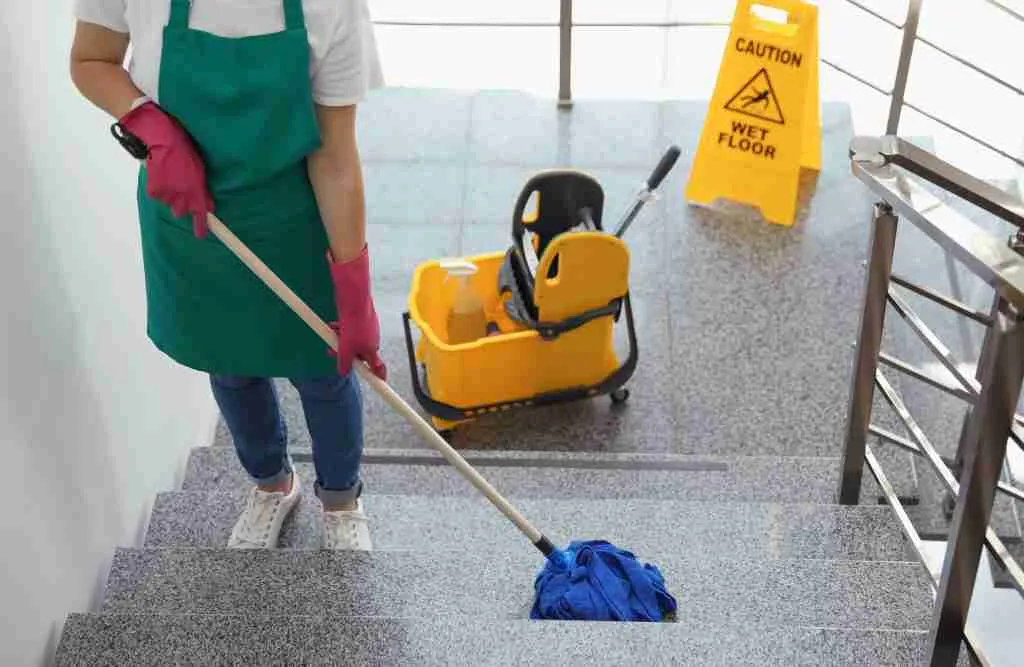 Person mopping stairs with caution sign and cleaning cart nearby.