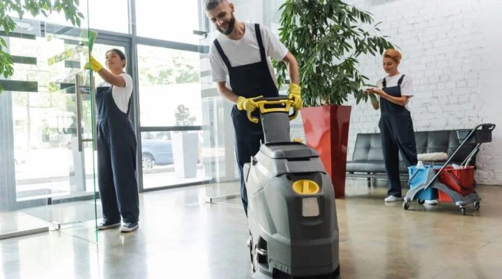 Janitors cleaning a bright office, one using a floor polishing machine.