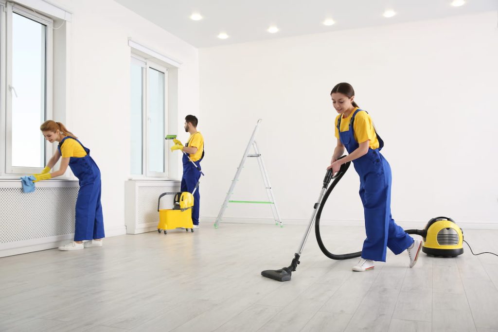 Three individuals in blue overalls diligently cleaning a room, showcasing teamwork and attention to detail.